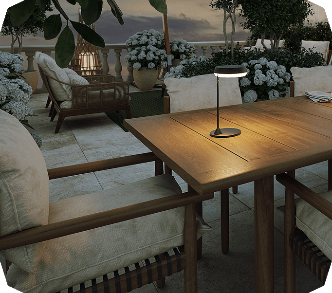 Cozy outdoor terrace at dusk with wooden table, cushioned chairs, modern table lamp, and lush potted white flowers.